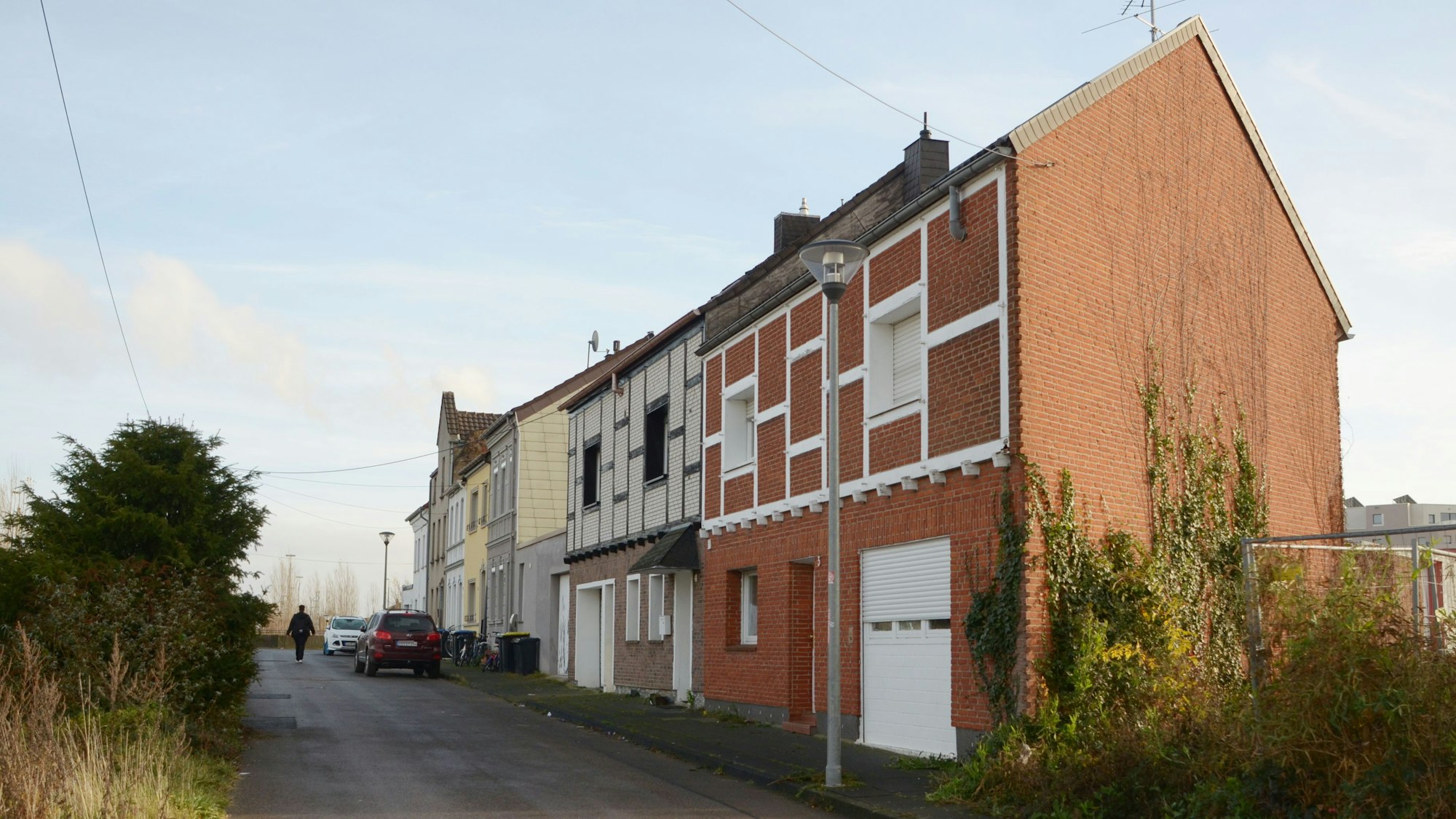 Das Bild zeigt eine Häuserreihe, im Hintergrund geparkte Autos und ein Fúßgänger.