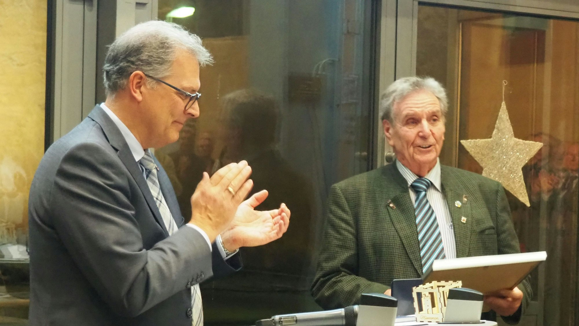 André Heinrichs (r.) hält eine gerahmte Urkunde in den Händen, Bürgermeister Ulf Hürtgen applaudiert.
