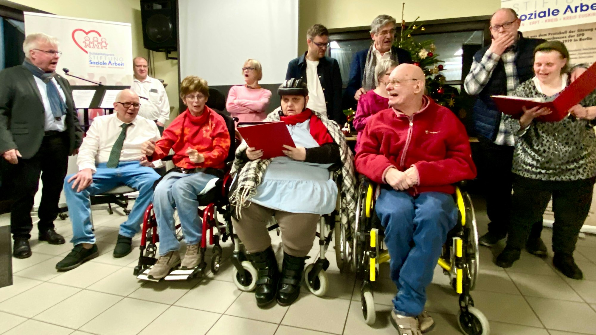 Eine Gruppe von Menschen mit und ohne Behinderung stehen und sitzen beieinander und singen.