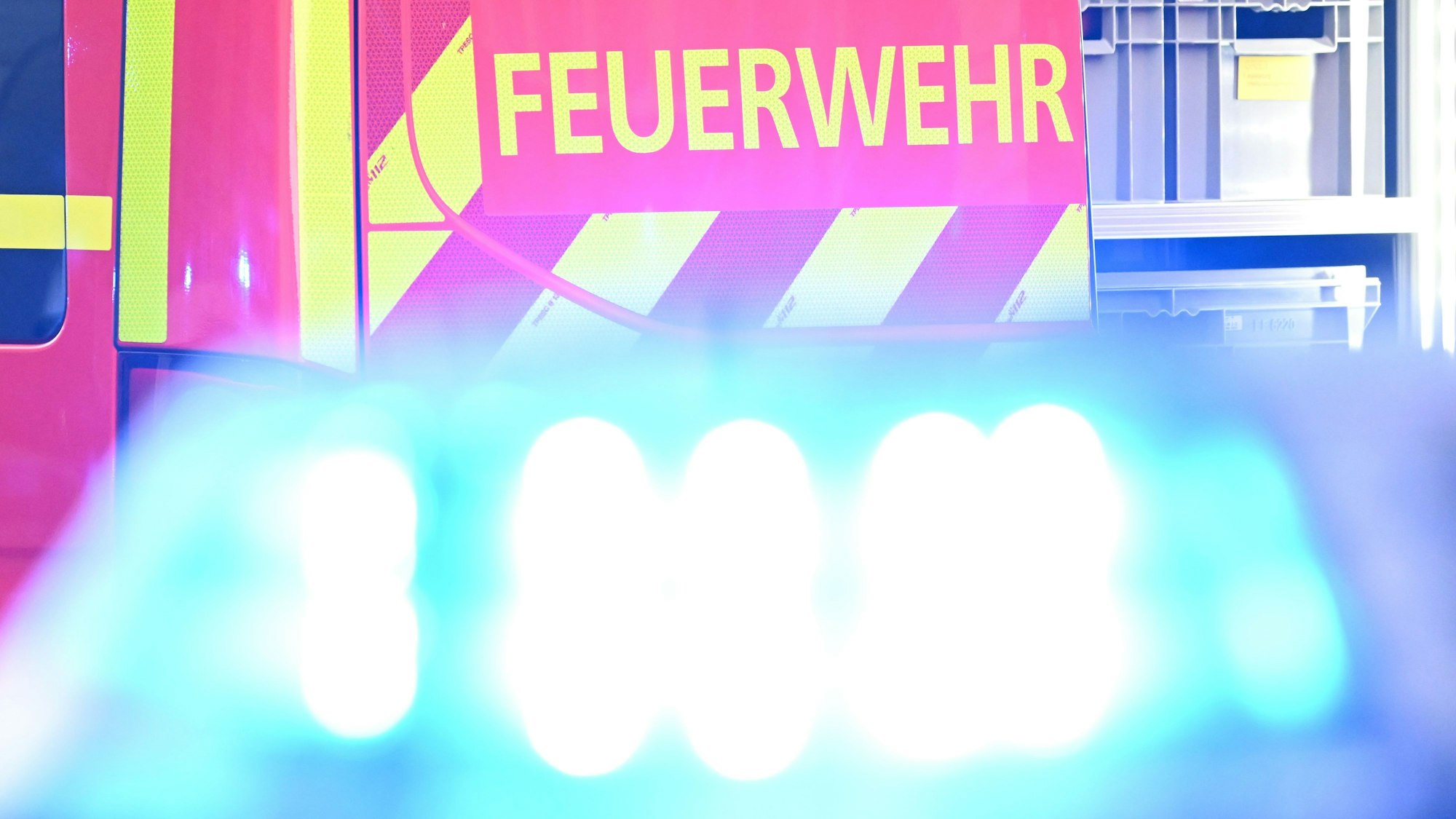 Ein Fahrzeug der Feuerwehr steht bei einem Einsatz auf einer Straße, während im Vordergrund das Blaulicht eines Polizeifahrzeugs zu sehen ist.