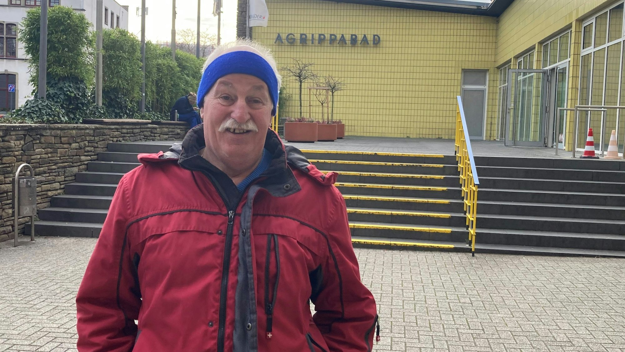 Ein älterer Mann steht vor einem Schwimmbad.