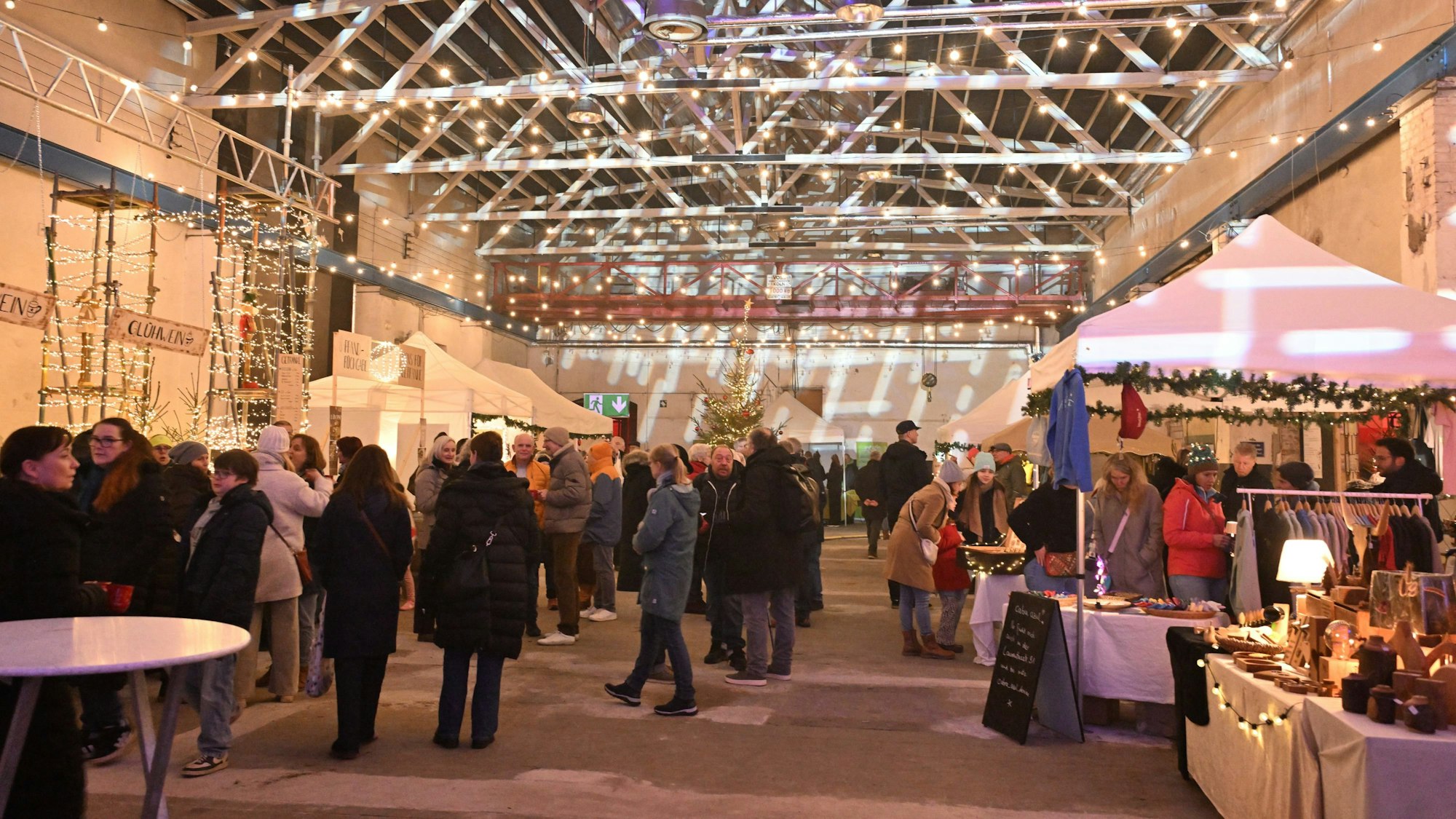 Eine Menschenmenge bummelt in einem stimmungsvoll beleuchteten Saal auf einem Weihnachtsmarkt.