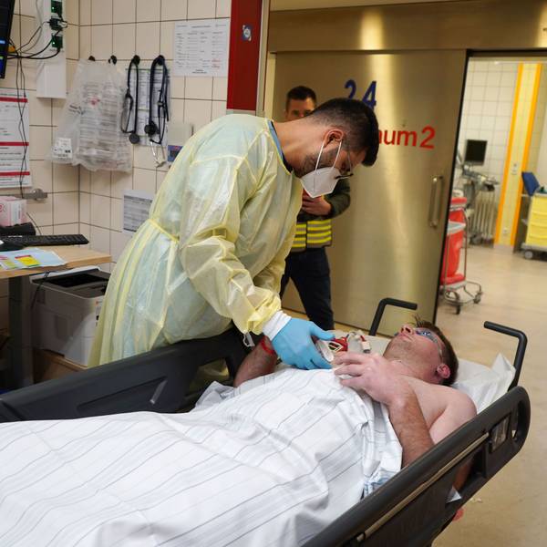 Ein Patient liegt auf einer Liege, während ein Krankenhaus Mitarbeiter über ihn gebeugt ist.