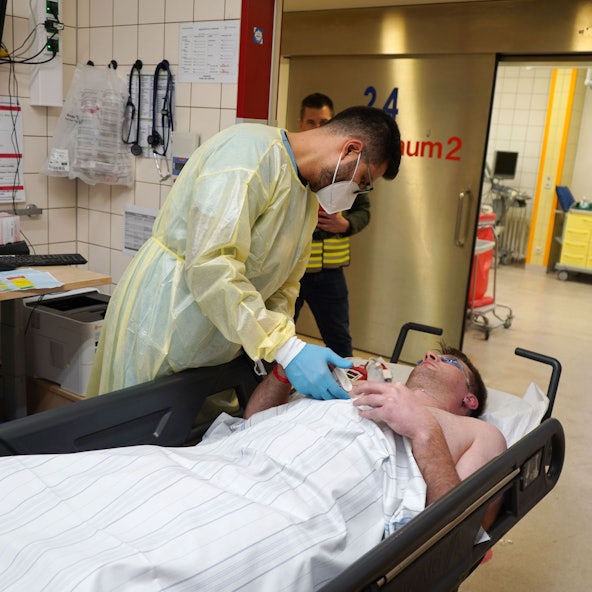 Ein Patient liegt auf einer Liege, während ein Krankenhaus Mitarbeiter über ihn gebeugt ist.