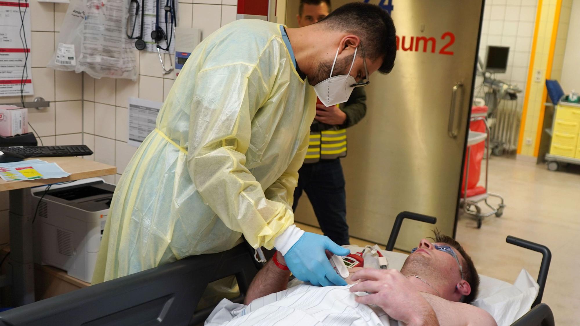 Ein Patient liegt auf einer Liege, während ein Krankenhaus Mitarbeiter über ihn gebeugt ist.