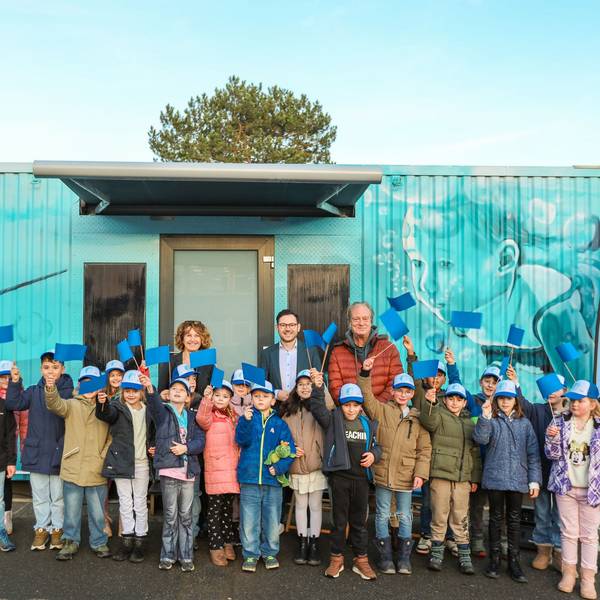 Viele Kinder winken mit blauen Fähnchen, dahinter stehen drei Erwachsene.
