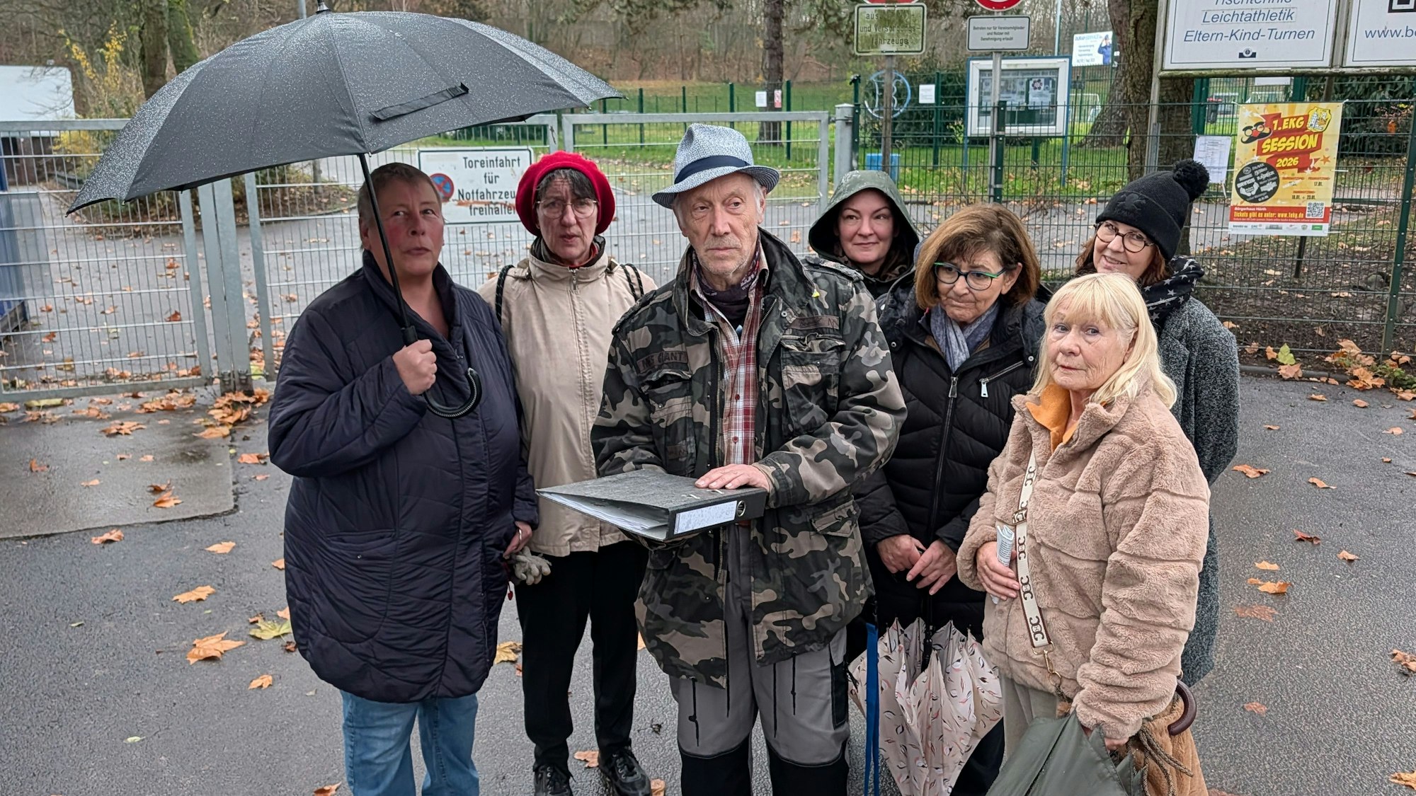 Das Foto zeigt eine Gruppe von Menschen mit einem Aktenordner vor dem Sportplatz in Efferen.