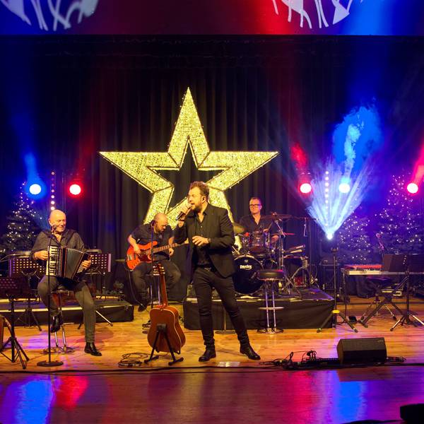 Das Bild zeigt die fünfköpfige Musikgruppe auf der weihnachtlich dekorierten Bühne.