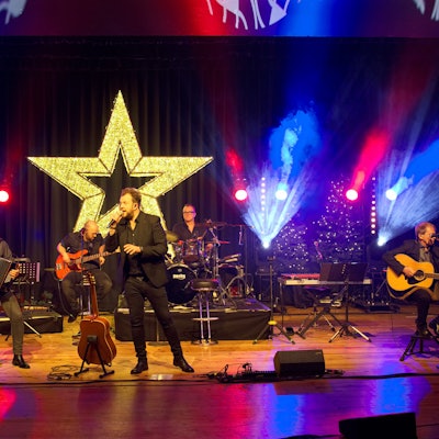 Das Bild zeigt die fünfköpfige Musikgruppe auf der weihnachtlich dekorierten Bühne.