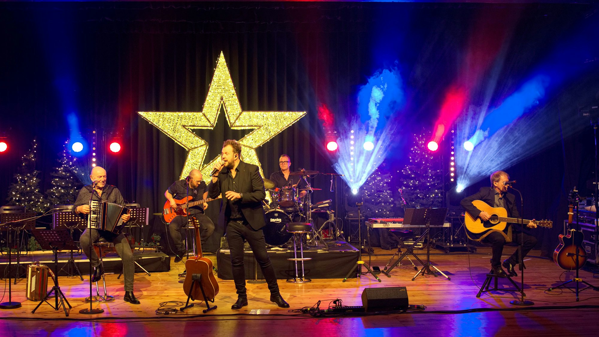 Das Bild zeigt die fünfköpfige Musikgruppe auf der weihnachtlich dekorierten Bühne.