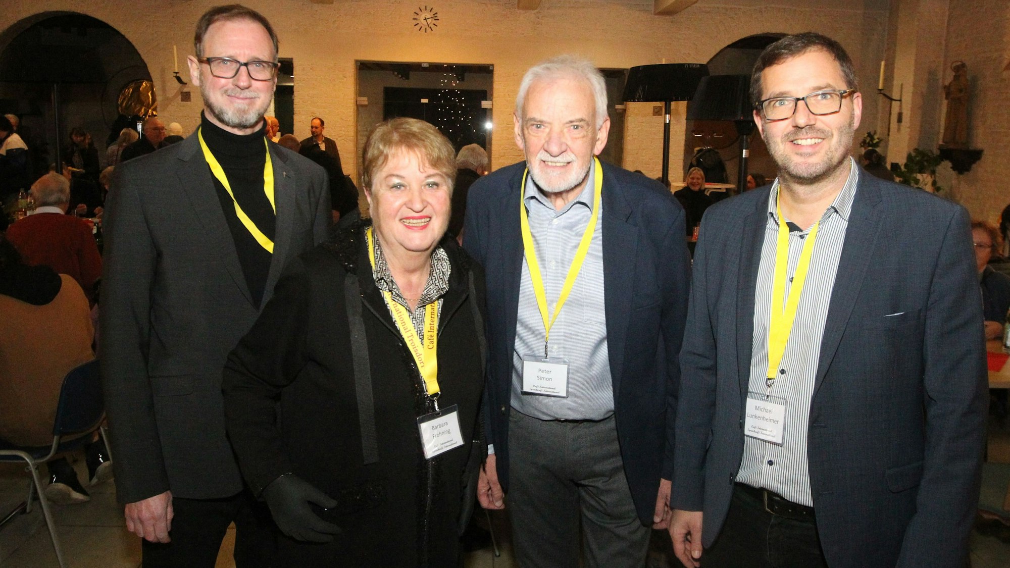 Drei Männer und eine Frau; alle tragen gelbe Bänder um den Hals, an denen Namensschilder hängen.