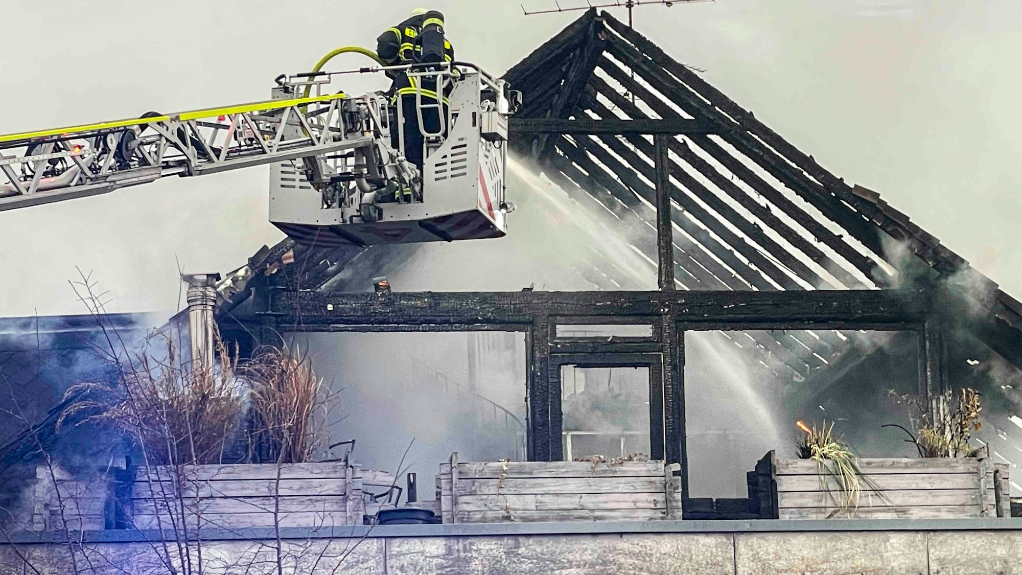 Das Bild zeigt den bereits ausgebrannten Dachstuhl. Die Feuerwehr löscht von der Drehleiter aus.