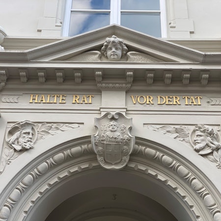 Zu sehen ist eine Inschrift am Brühler Rathaus. Sie lautet „Halte Rat vor der Tat“.