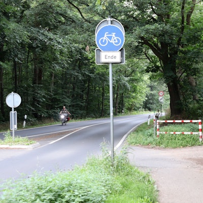 An einer Straße liegt ein Radweg, der an einer Schranke endet.