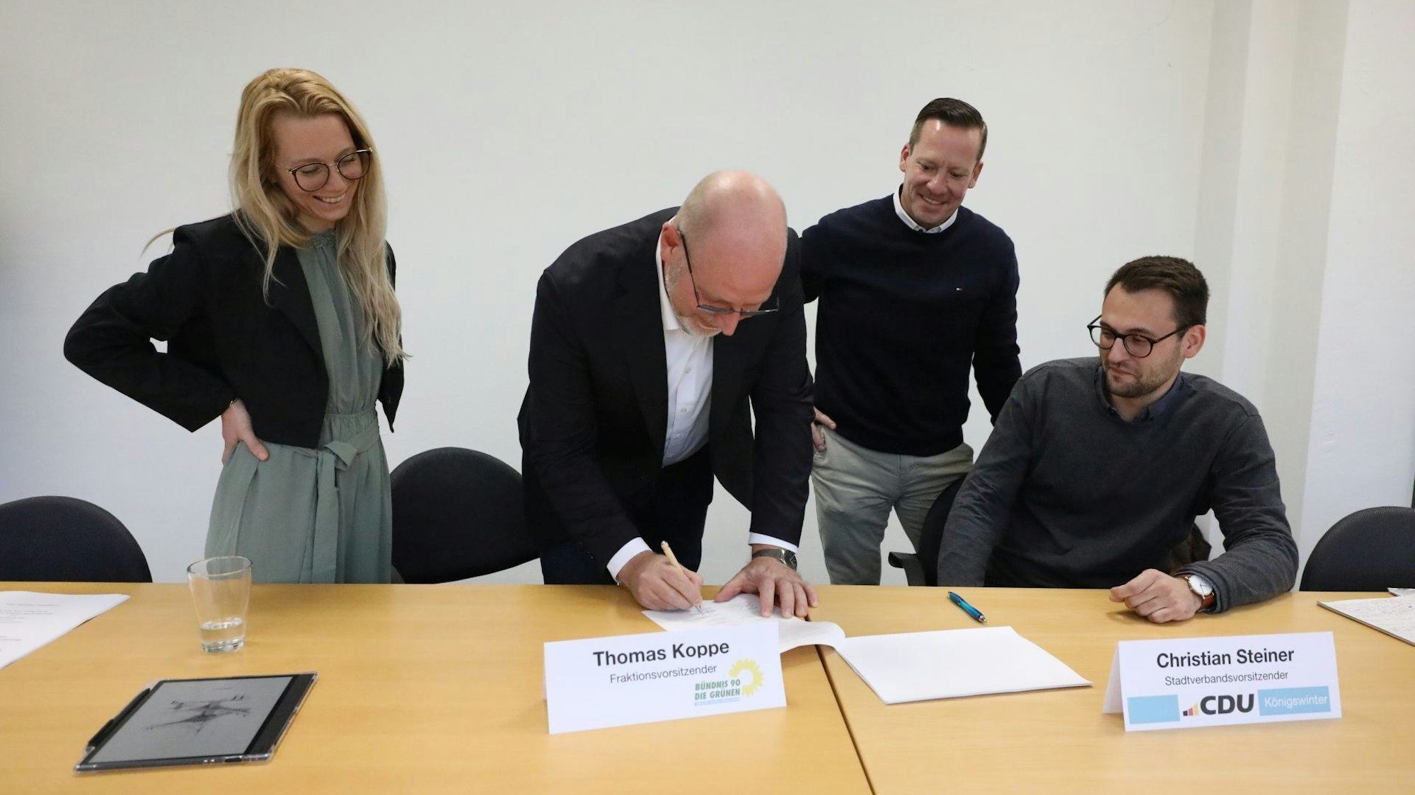 Eine Frau und drei Männer an einem Tisch, einer unterschreibt ein Papier.