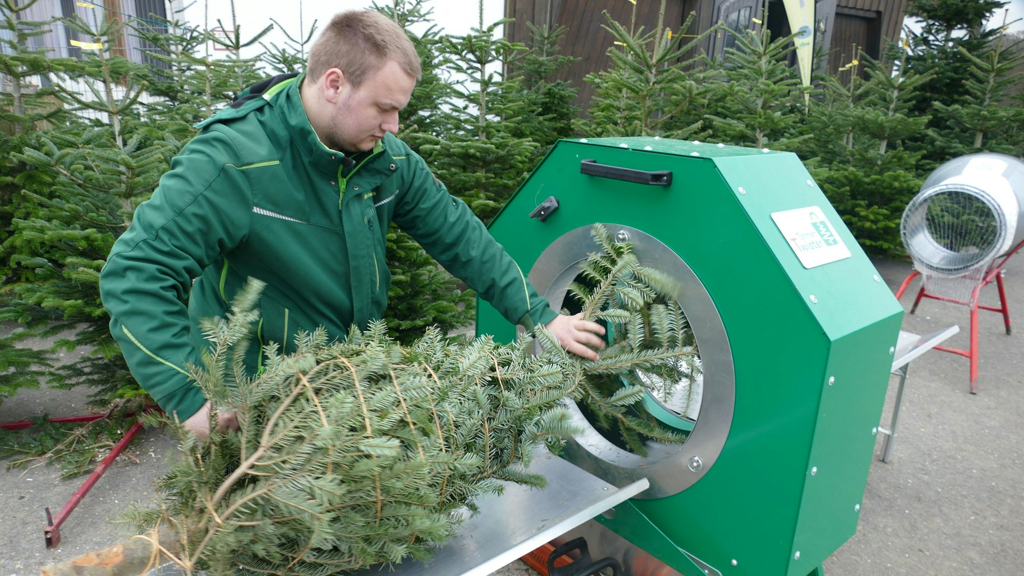 Finn Schmitz aus Lohmar an einer Maschine, die Weihnachtsbäume nicht mit einem Netz, sondern Jute-Kordeln umwickelt.