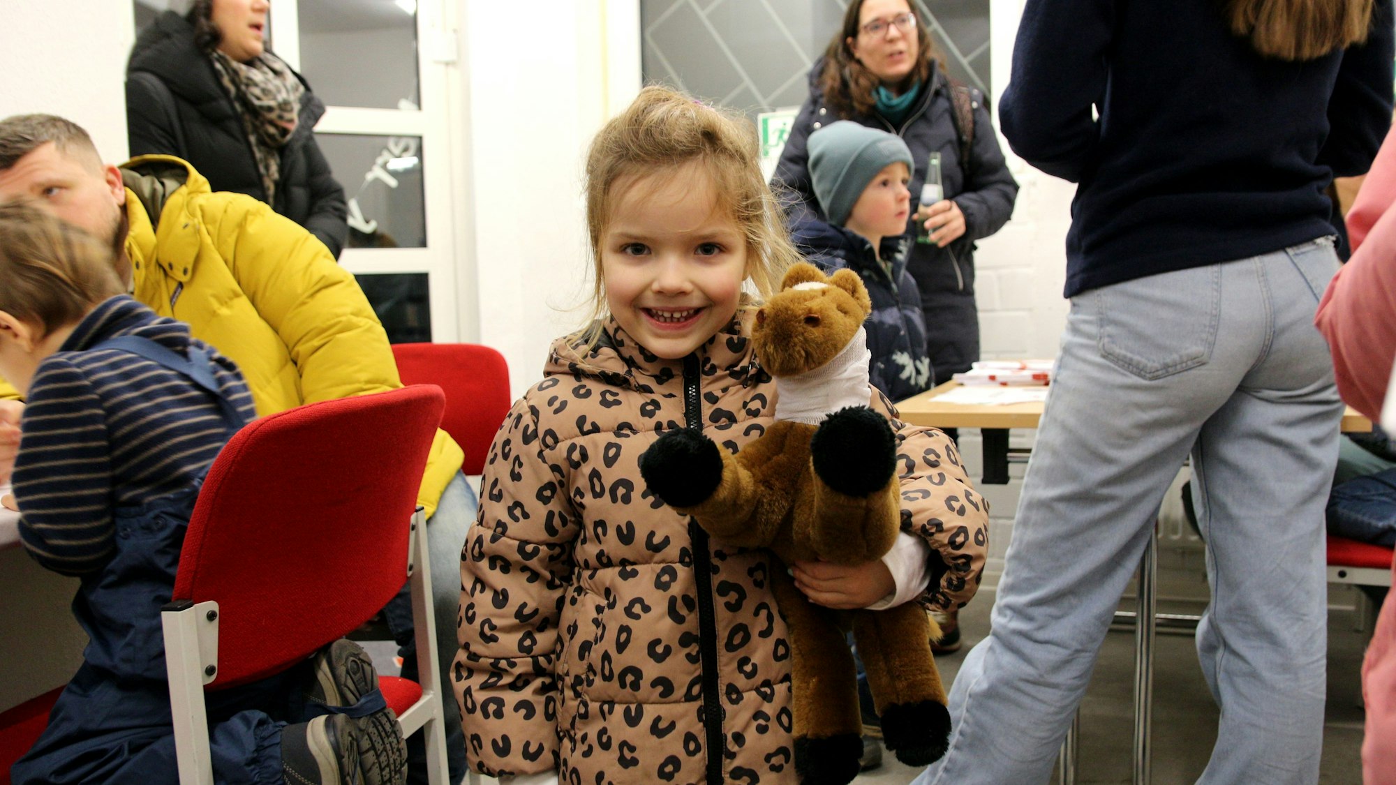 Ein Mädchen lächelt, es hält ein Stofftier im Arm. Das Pferd hat einen Verband um den Hals.