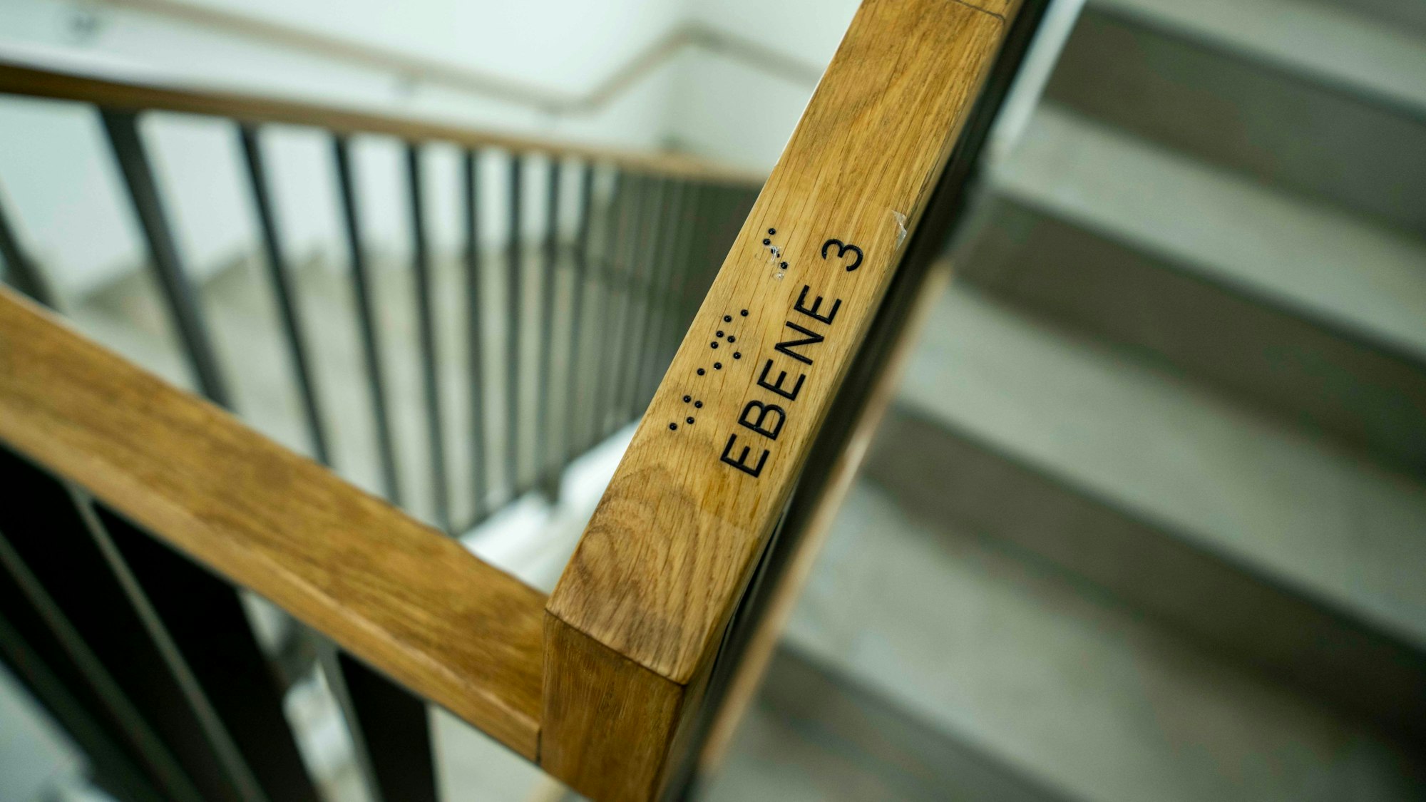 Das Bild zeigt ein Treppengeländer mit einem Hinweis für blinde Menschen.