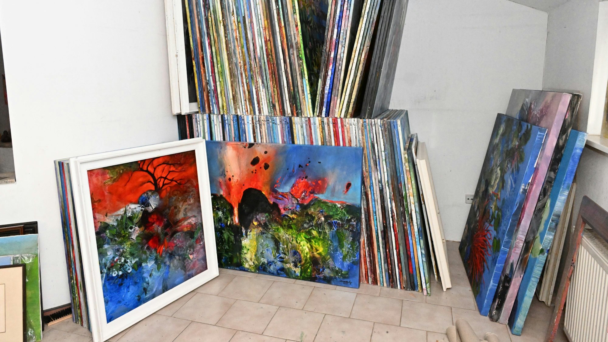 Viele Bilder stehen als Stapel gegen eine Wand gelehnt.