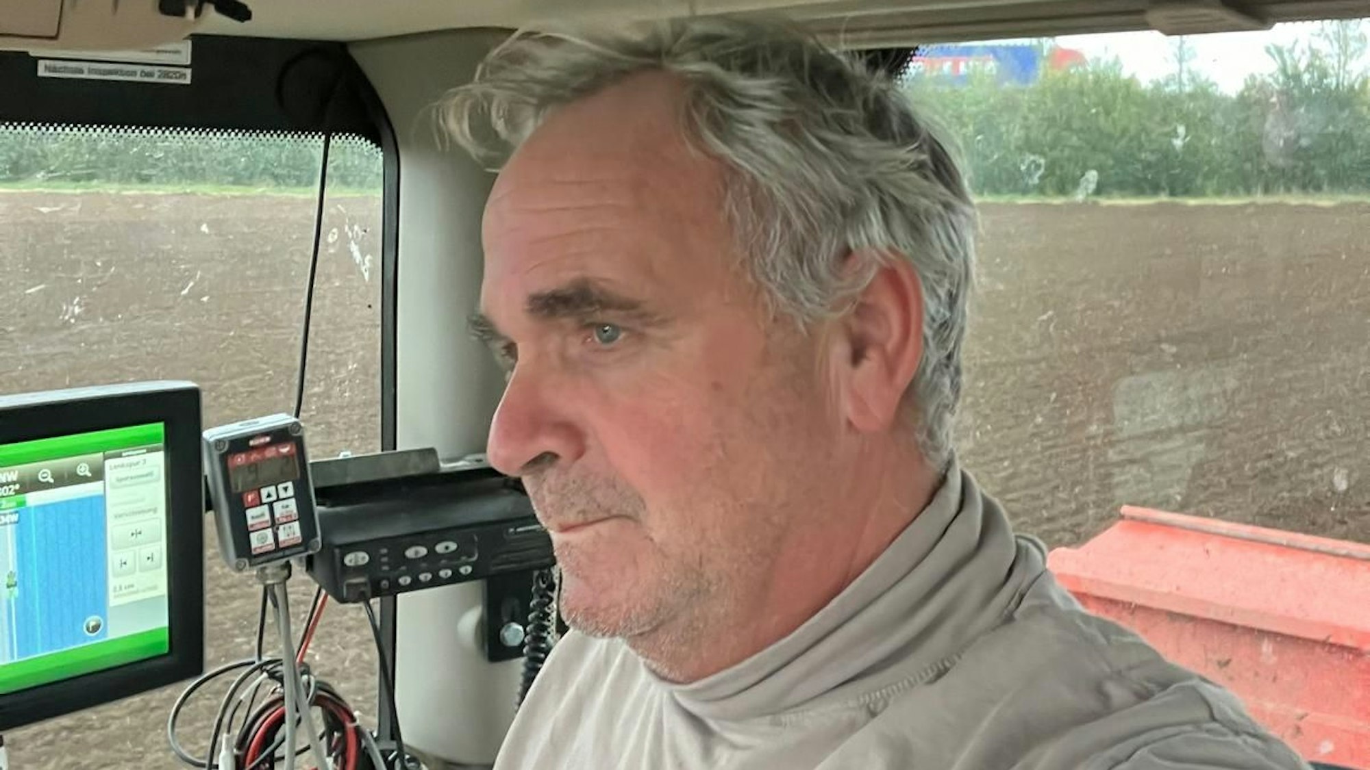 Zu sehen ist ein Landwirt in einem Traktor auf einem Feld.