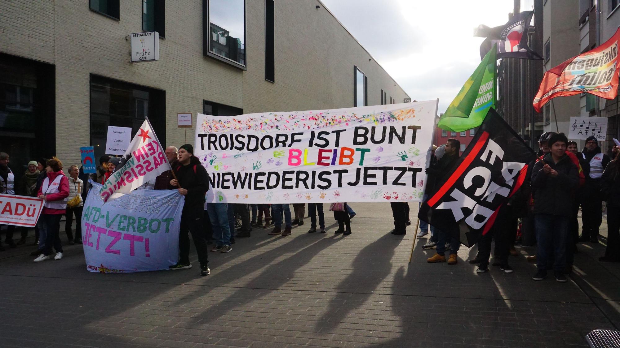 Ein großes Transparent mit der Aufschrift „Troisdorf ist/bleibt bunt“ und dem Hashtag „Nie wieder ist jetzt“ dominiert die Gruppe der Demonstrierenden.