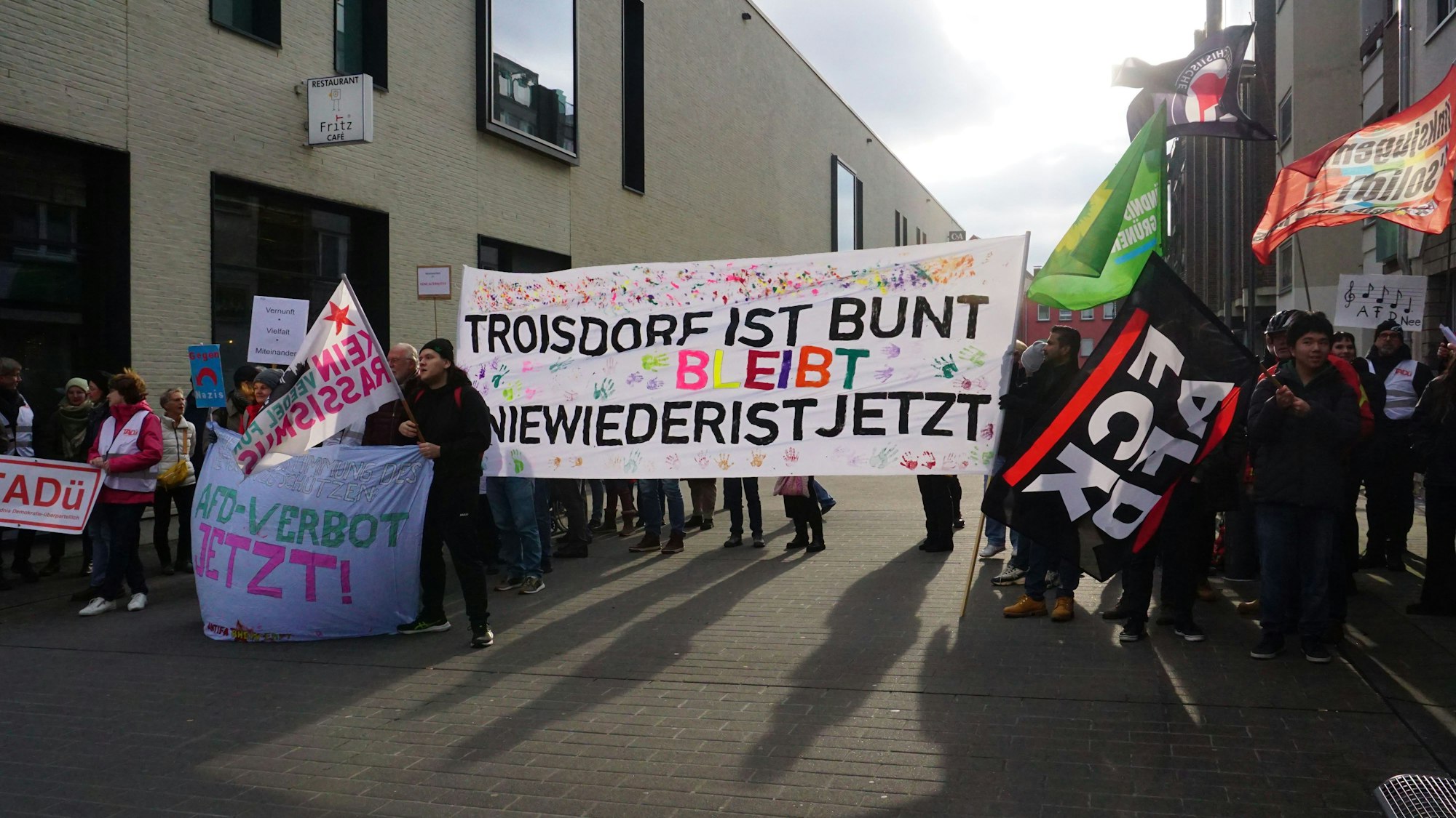 Ein großes Transparent mit der Aufschrift „Troisdorf ist/bleibt bunt“ und dem Hashtag „Nie wieder ist jetzt“ dominiert die Gruppe der Demonstrierenden.