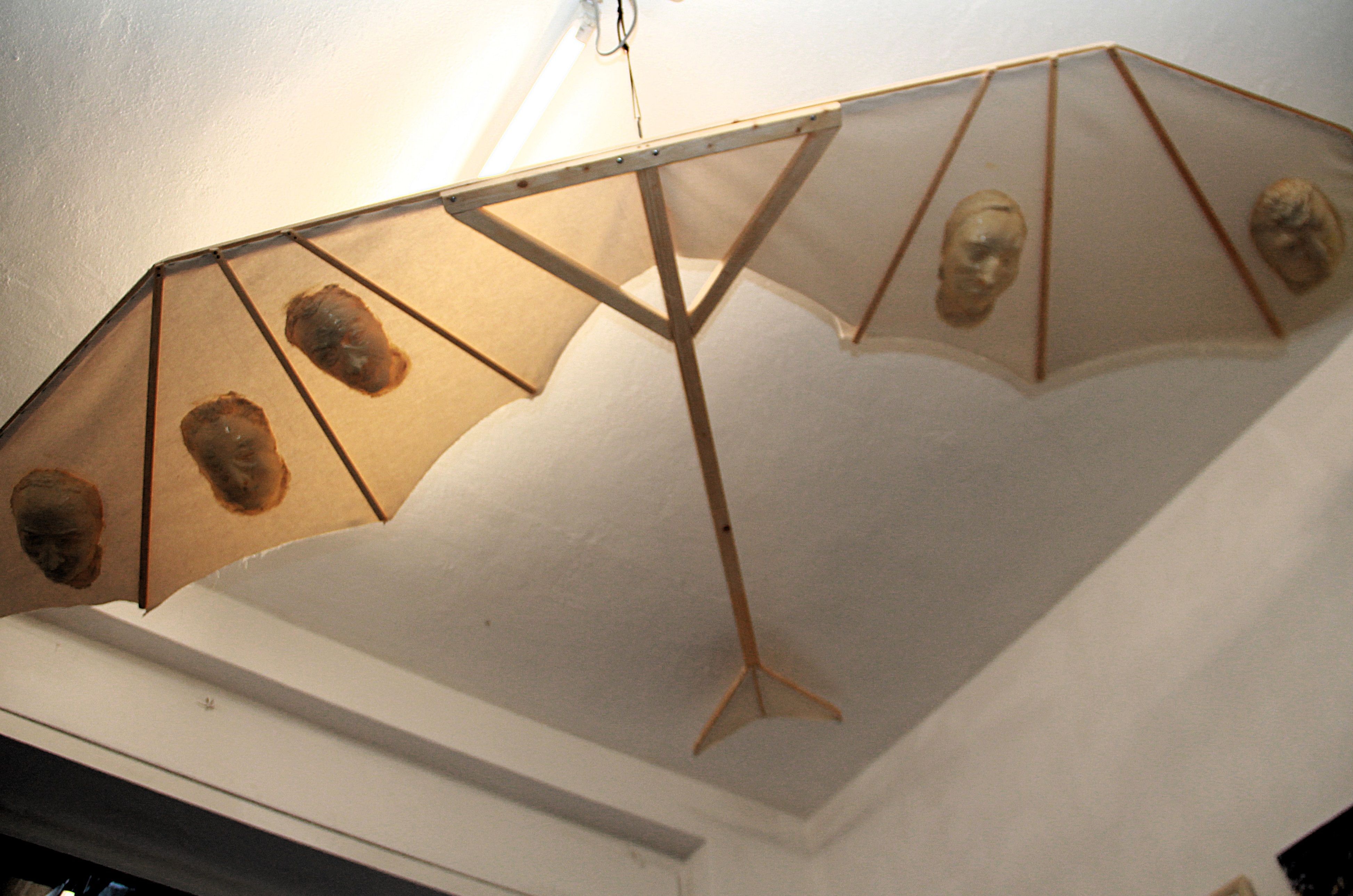 Eine Art Drachen mit einem Holzgestell ist an der Decke eines Altbau-Raumes befestigt.