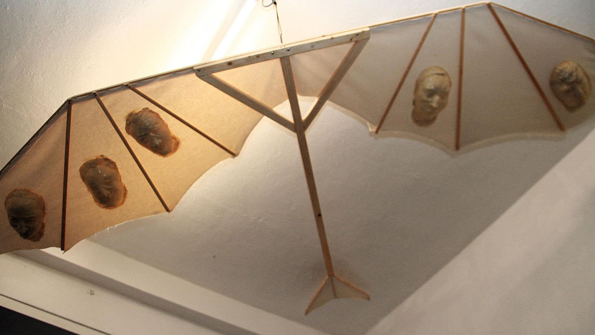 Eine Art Drachen mit einem Holzgestell ist an der Decke eines Altbau-Raumes befestigt.