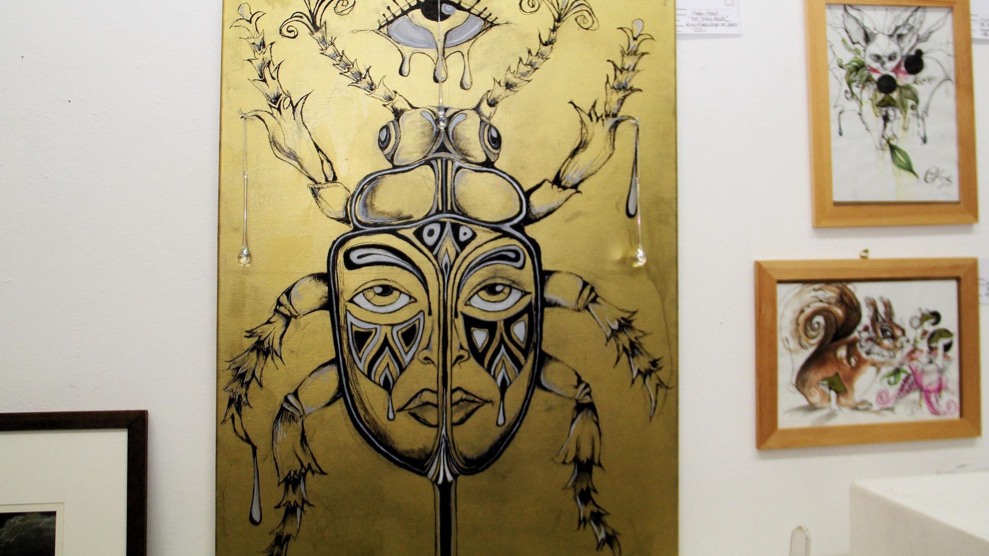 Ein großformatiges zeigt eine Maske, es ist in Goldtönen gehalten.