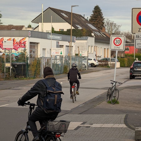 Das Foto zeigt zwei Radfahrer, die von der Kaulardstraße auf die Straße „Zum Komarhof“ abgebogen sind.