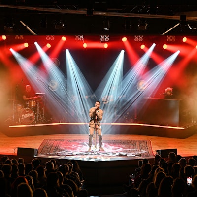 Der Musiker Mo-Torres steht von mehreren Scheinwerfern angeleuchtet auf einer Bühne. Das Publikum vor ihm ist in Umrissen zu sehen.