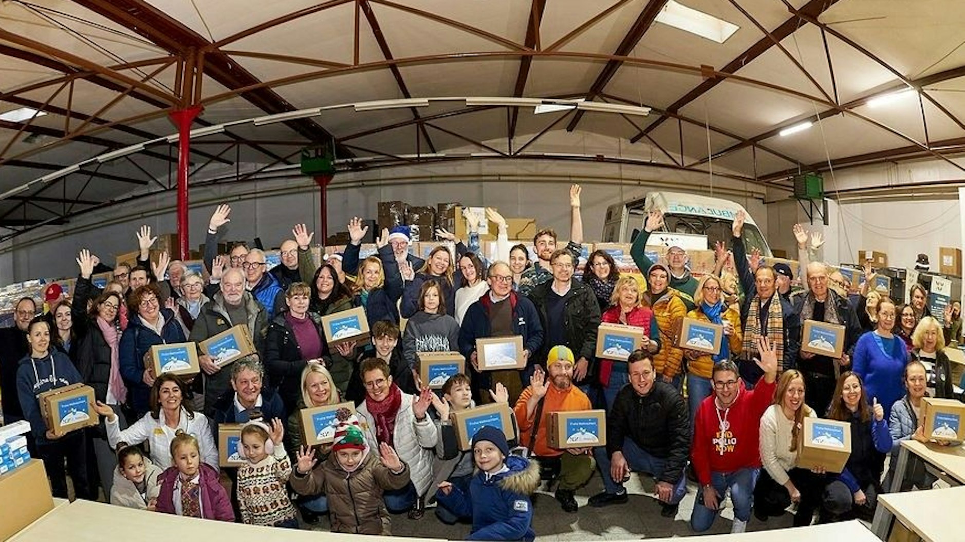 Zu sehen sind Erwachsene und viele Kinder, die Geschenkkartons in ihren Händen halten.