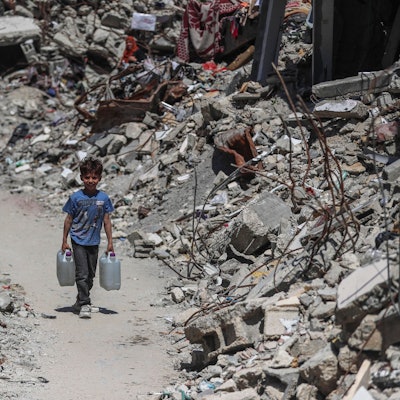 Das Symbolbild zeigt einen palästinensischen Jungen, der Wasser im Flüchtlingslager Jabalia im nördlichen Gazastreifen holt. Links und rechts von ihm türmt sich der Schutt zerstörter Häuser.