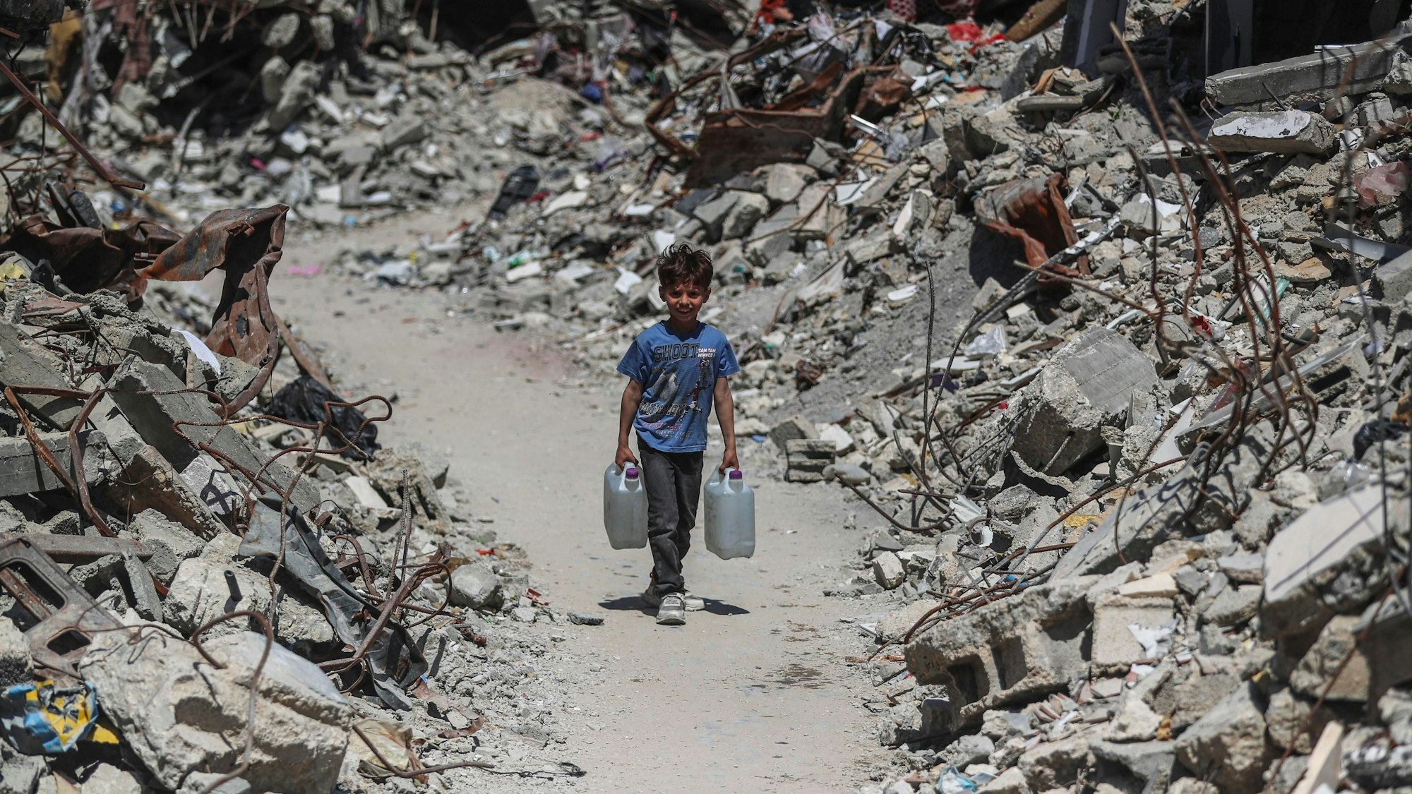 Das Symbolbild zeigt einen palästinensischen Jungen, der Wasser im Flüchtlingslager Jabalia im nördlichen Gazastreifen holt. Links und rechts von ihm türmt sich der Schutt zerstörter Häuser.