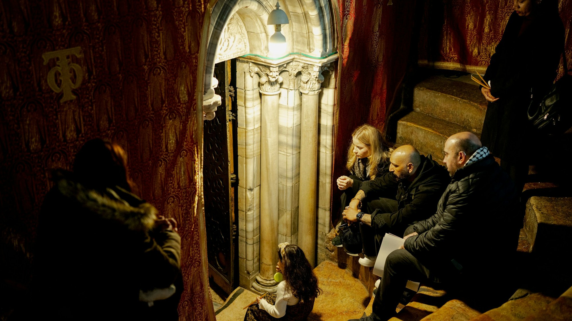 dpatopbilder - 21.12.2025, Palästinensische Gebiete, Bethlehem: Christen sitzen auf den Stufen der Grotte unter der Basilika, dem angeblichen Geburtsort Jesu Christi, in der Geburtskirche in der Stadt Bethlehem im Westjordanland, wenige Tage vor den Weihnachtsfeierlichkeiten. Foto: Erik Marmor/dpa +++ dpa-Bildfunk +++