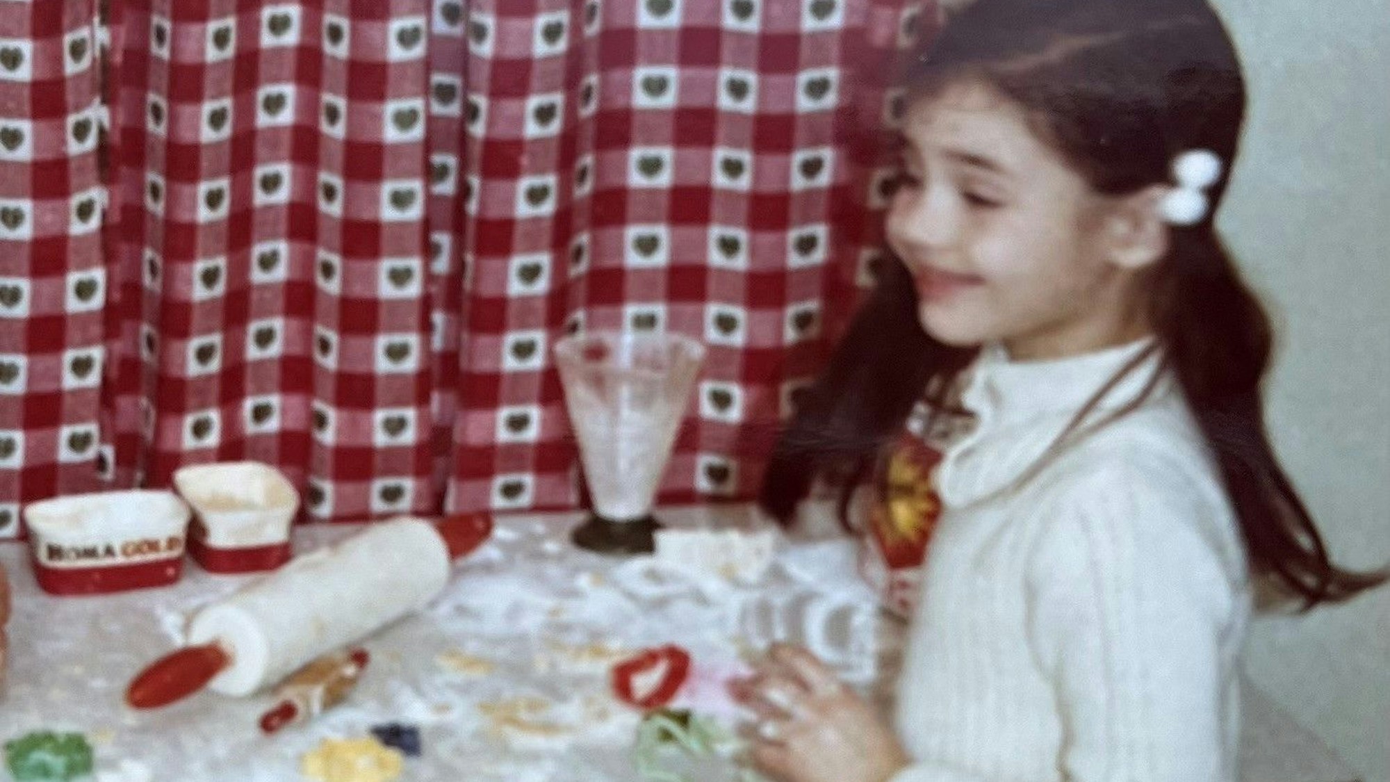 Ein Mädchen steht grinsend vor einem Tisch auf dem Backutensilien und Mehl liegen.