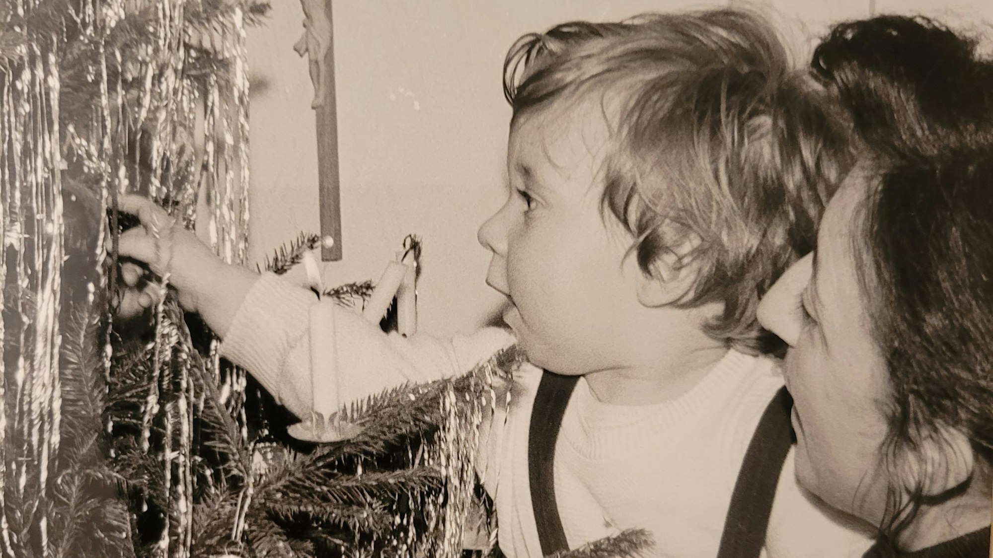 Ein kleiner Junge wird von seiner Mutter auf dem Arm getragen und bewundert das Lametta am Weihnachtsbaum.