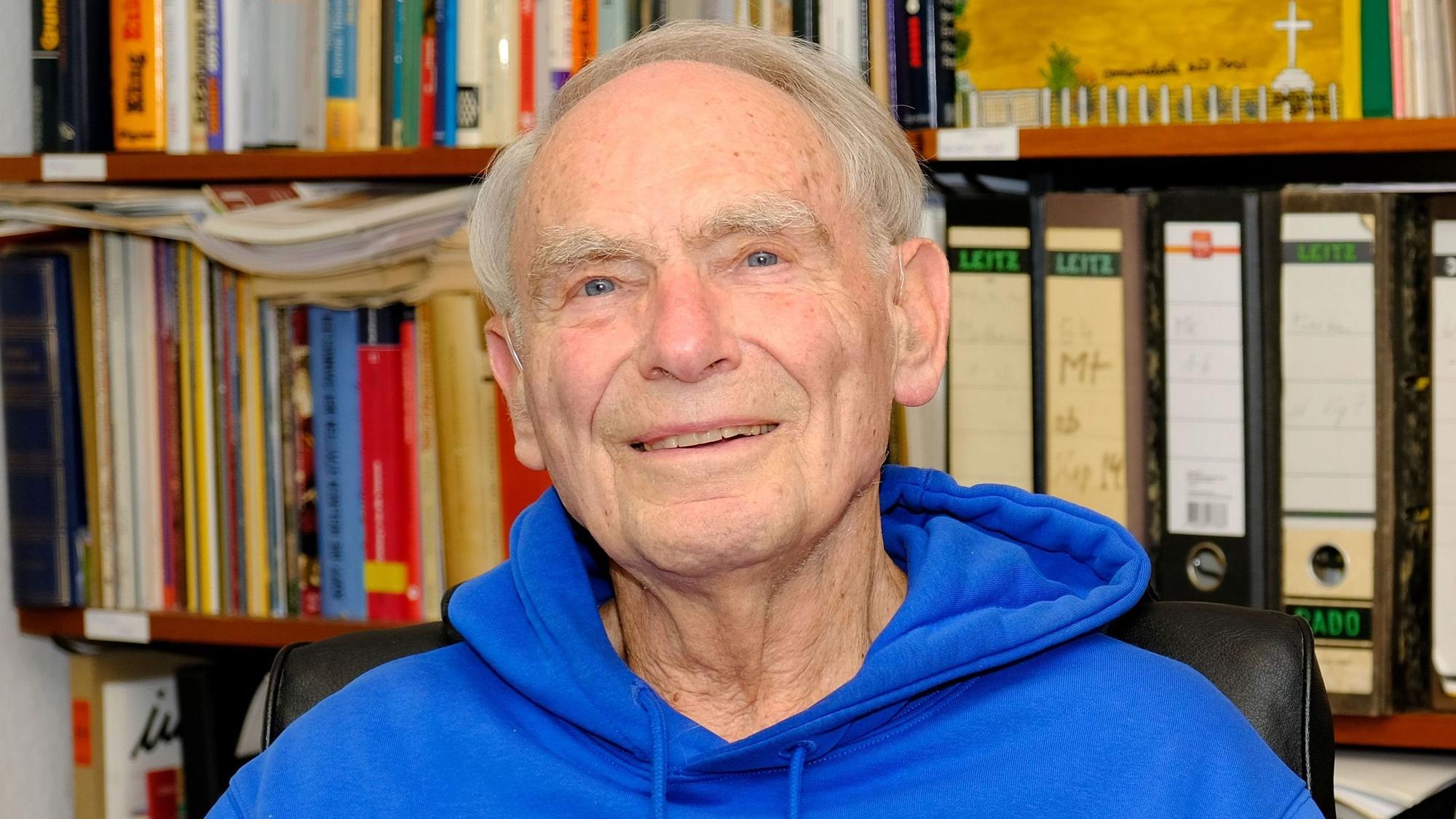 Dr. Herbert Kaefer (87), Pfarrer im Ruhestand aus Gemünd, sitzt in einem kobaltblauen Hoodie in seinem Arbeitszimmer.