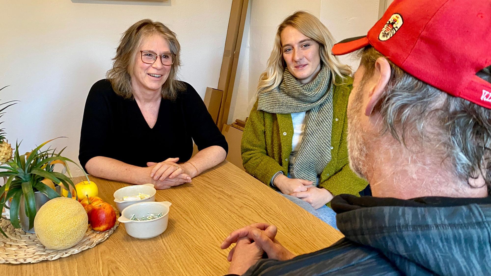 Maria Surges-Brilon und Gina Raths sitzen am Tisch und sind im Gespräch mit dem Bewohner, den man nur von hinten sieht.