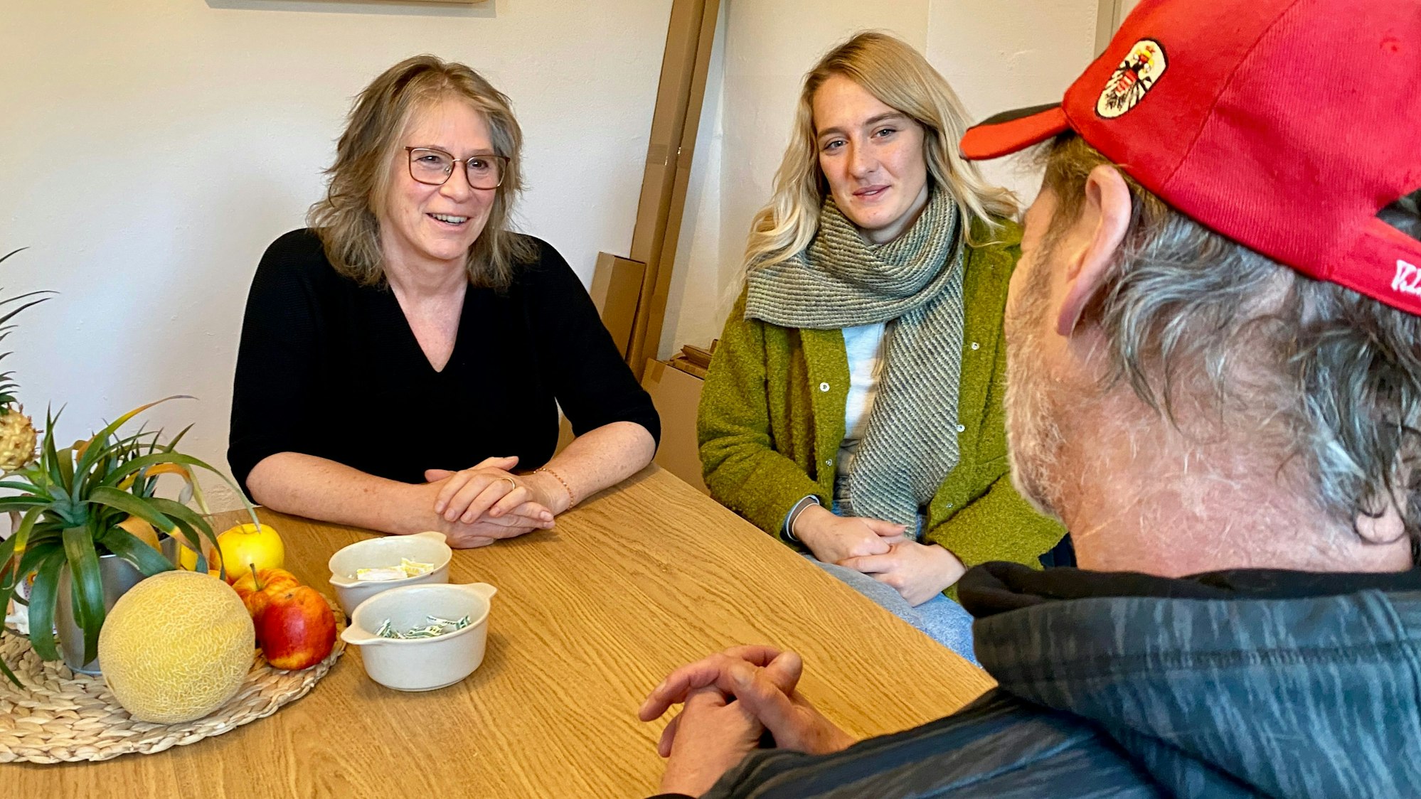 Maria Surges-Brilon und Gina Raths sitzen am Tisch und sind im Gespräch mit dem Bewohner, den man nur von hinten sieht.