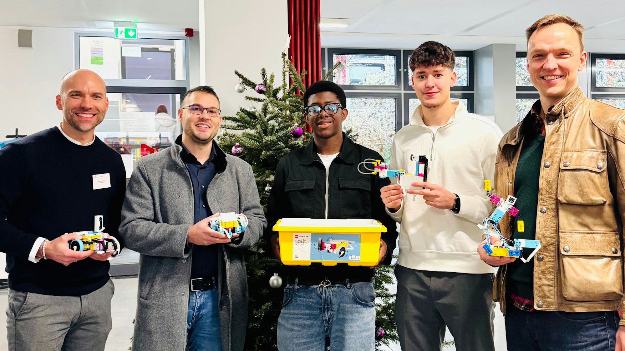 Drei Männer und zwei Jugendliche mit Lego-Bauteilen vor einem Weihnachtsbaum.