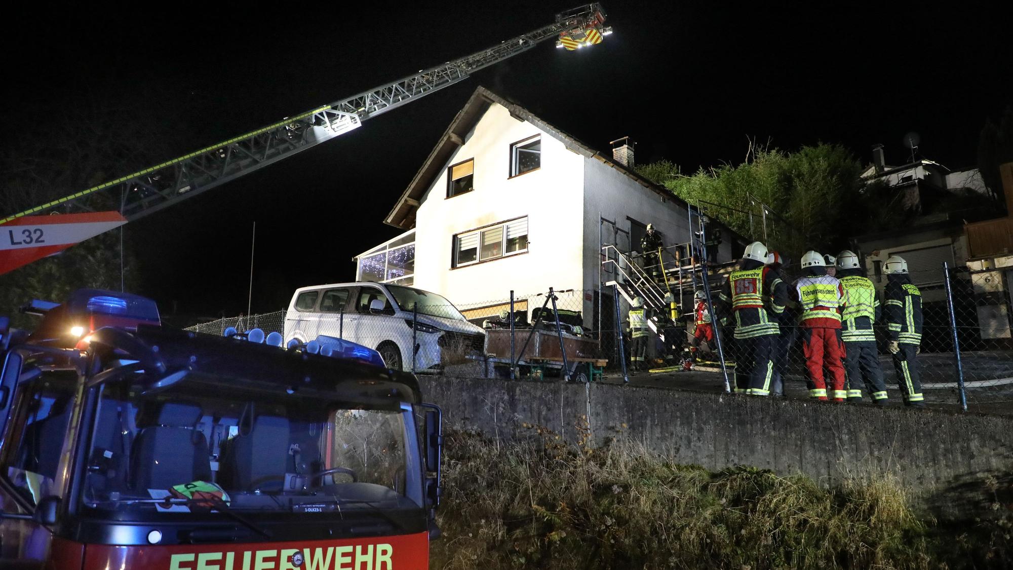 Eine Feuerwehrdrehleiter steht vor einem Haus, das offenbar gebrannt hat. Feuerwehrleute stehen davor.