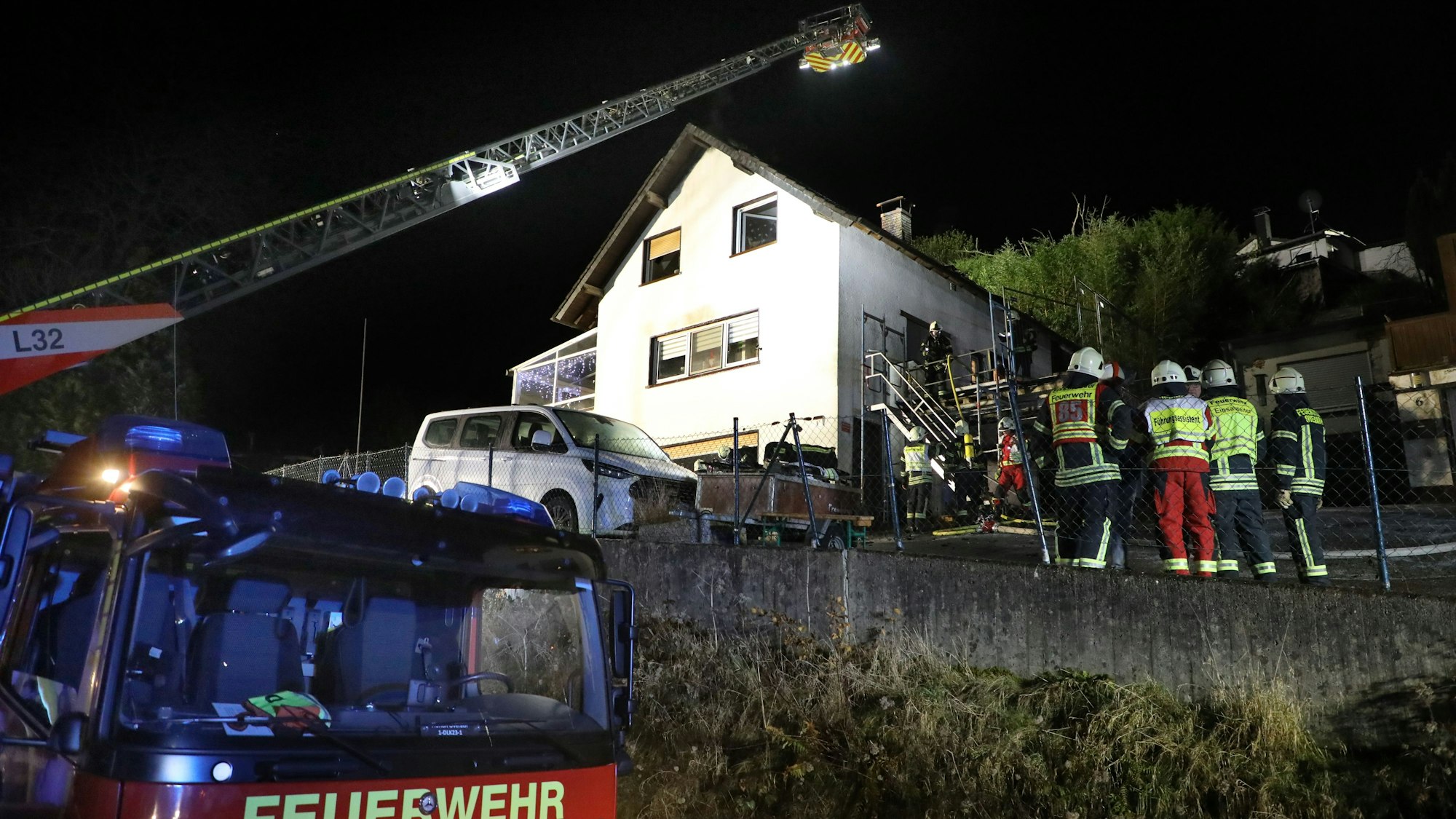 Eine Feuerwehrdrehleiter steht vor einem Haus, das offenbar gebrannt hat. Feuerwehrleute stehen davor.