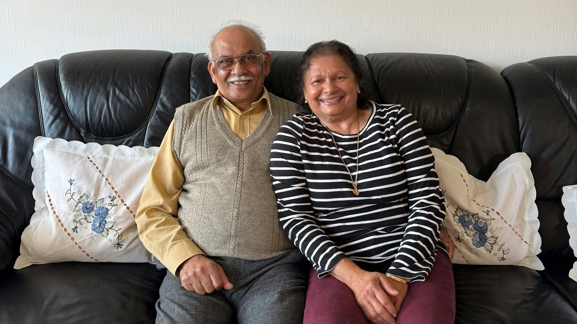 Ein Ehepaar sitzt nebeneinader auf einer schwarzen Couch.