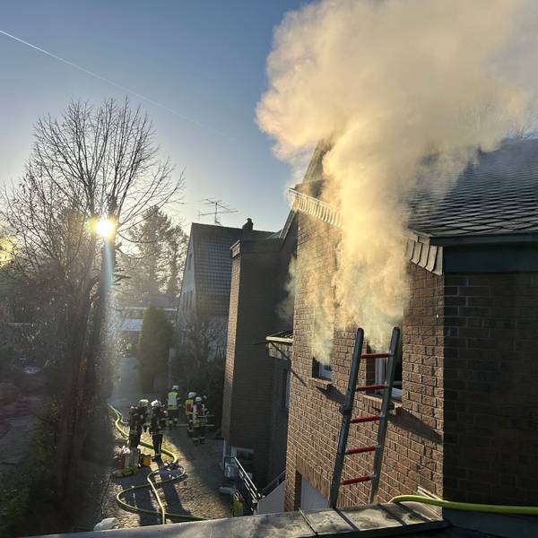 Es qualmt aus einem Fenster. Feuerwehrleute sind im Einsatz.