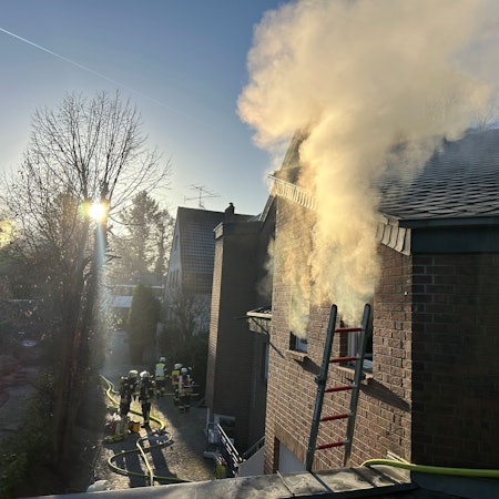 Es qualmt aus einem Fenster. Feuerwehrleute sind im Einsatz.