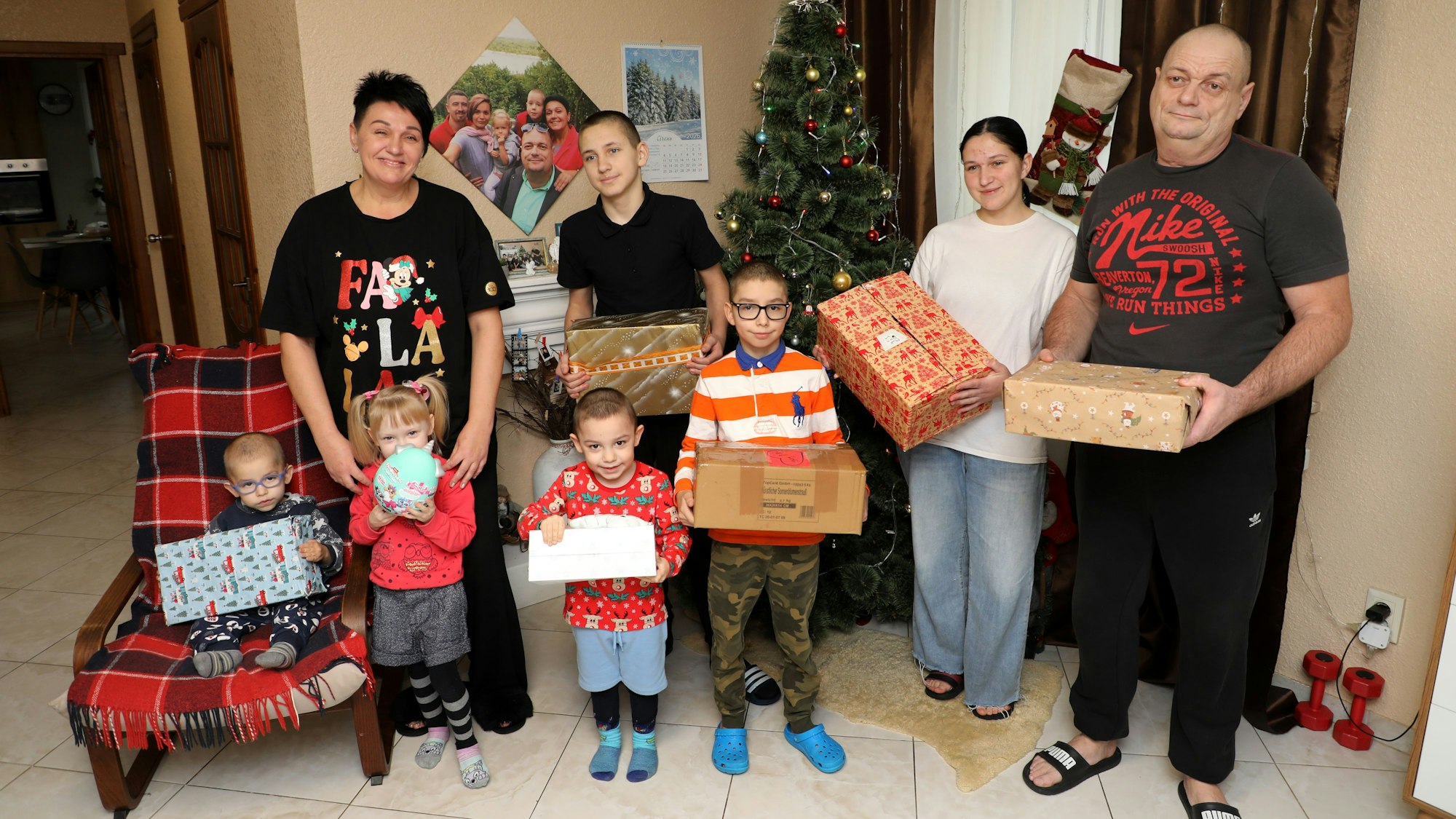 Eine Waisenhausfamilie steht mit Weihnachtsgeschenken in den Händen vor einem Weihnachtsbaum in ihrem Haus.