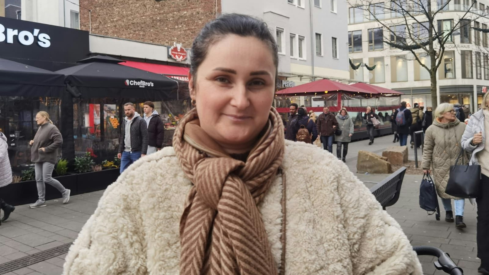 Eine junge Frau mit einem Schal um schaut leicht lächelnd in die Kamera.