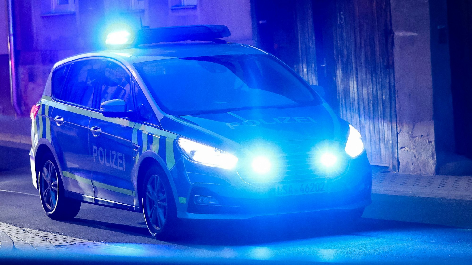Ein Fahrzeug der Polizei fährt mit Blaulicht am Abend durch eine enge Straße.