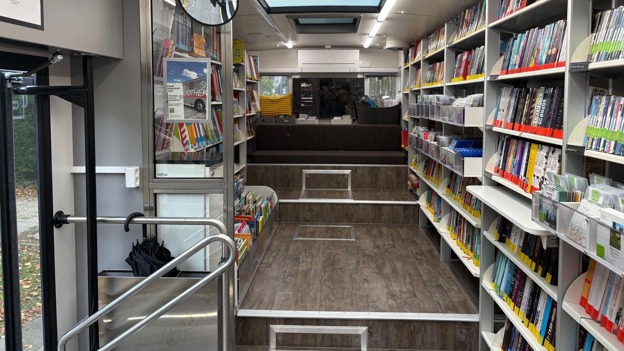 Die Inneneinrichtung der Busbibliothek: An den Seiten sind weiße Regale mit Büchern gefüllt, in der Mitte ein geräumiger Flur. Am Ende des Flurs ist eine Sitzgelegenheit.